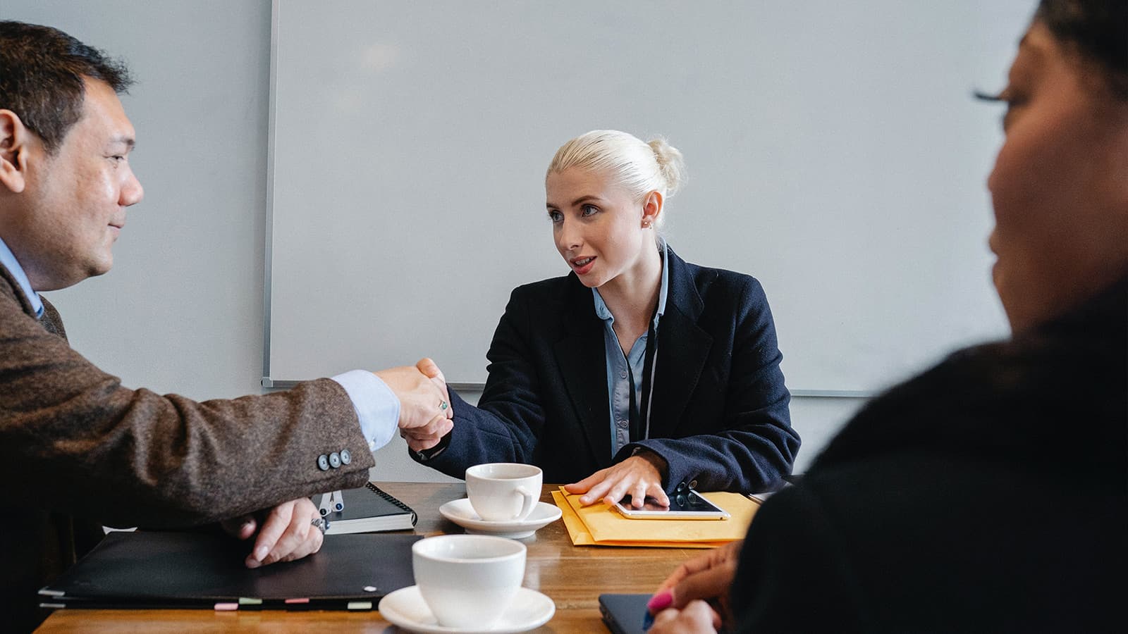2 people shaking hands over table, another looking