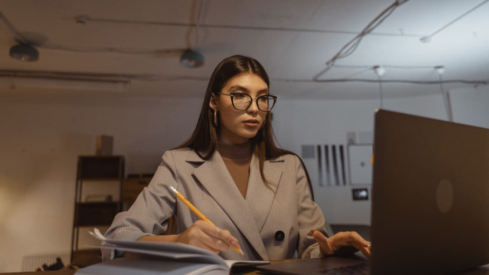 Woman in glasses making notes in front of laptop