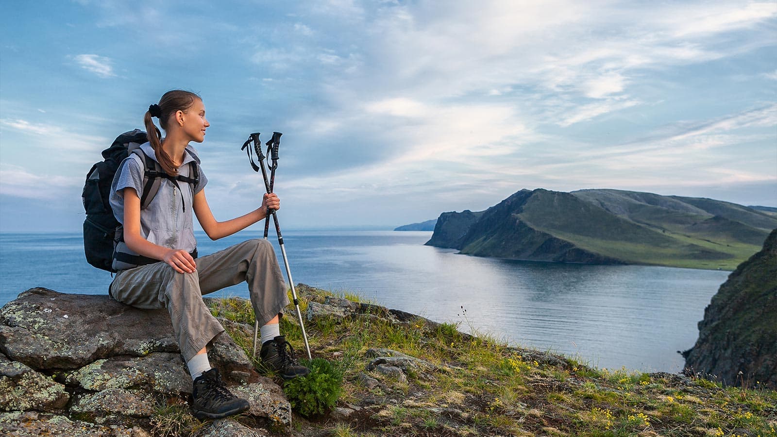 Woman with hiking gear resting on hill by a lake